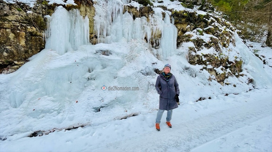 die Nomadin vor dem zugefrorener Wasserfall eines Zulaufes